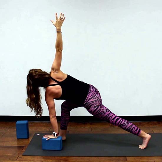 yoga teacher demonstrating crescent lunge with a twist, supported on a block