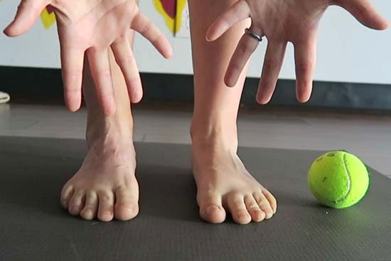 hands, feet and tennis ball on a yoga mat