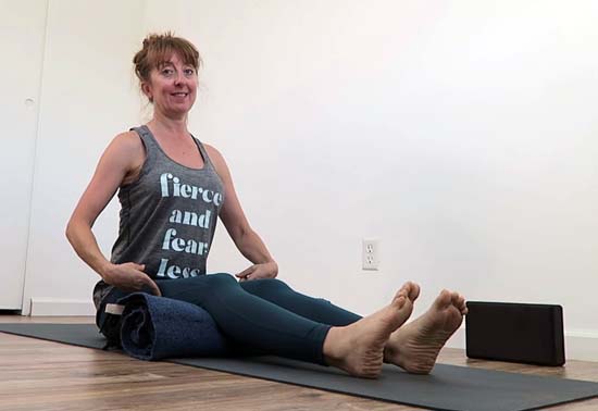 yoga teacher sitting in dandasana with knees bent and supported