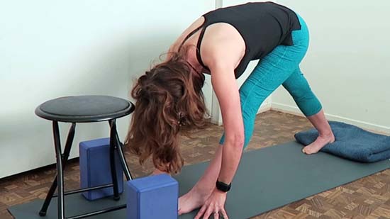 yoga teacher demonstrating pyramid pose with back heel elevated and supported