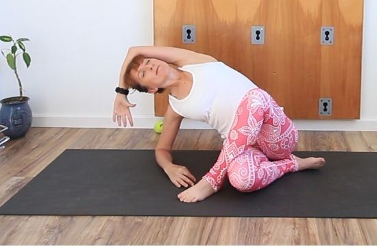 Yoga teacher on a mat wearing pink paisley leggings and white top