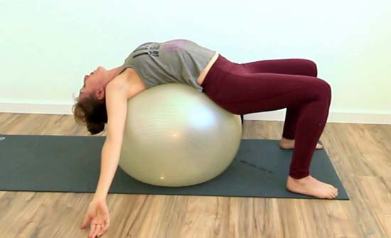 yoga teacher doing a backbend on a stability ball with knees bent and arms to side