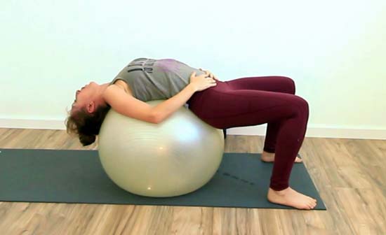 yoga teacher laying on a stability ball with knees bent