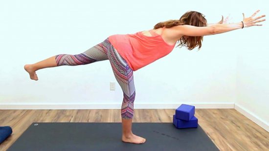 yoga teacher in warrior 3 pose with arms extended
