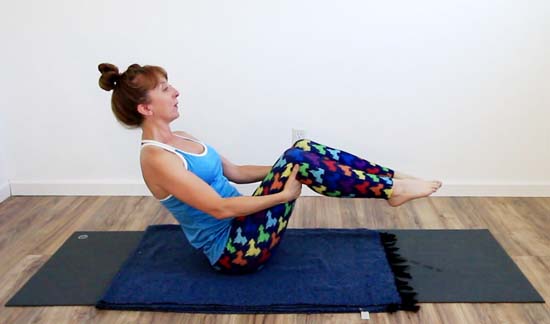 yoga teacher in boat pose with knees bent and hands behind thighs