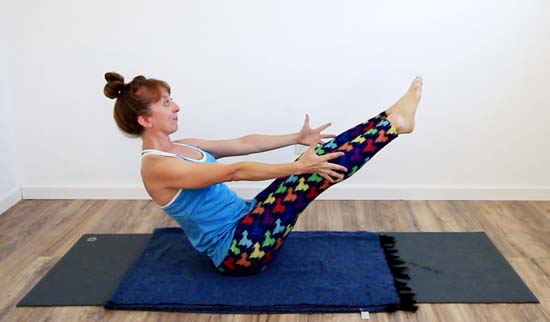 yoga teacher performing boat pose with both arms and legs extended