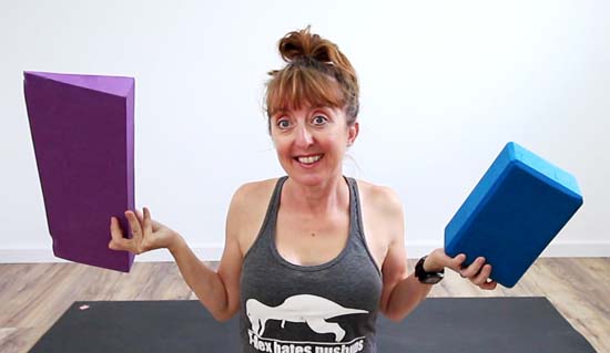 yoga teacher holding a yoga wedge and yoga block for comparison