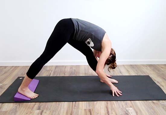 yoga teacher showing variation of pyramid pose with yoga wedge under the back foot