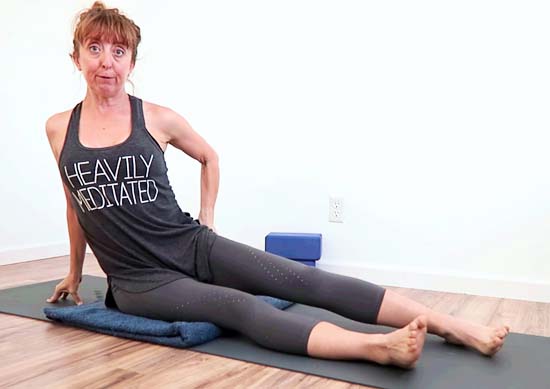 yoga teacher sitting with one hip elevated off the yoga mat