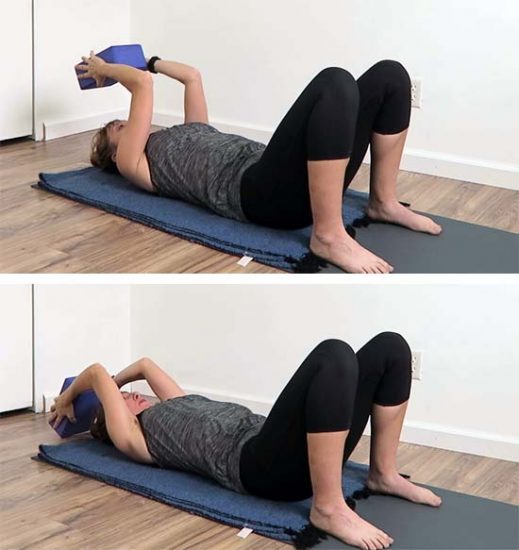Yoga teacher laying on a yoga mat using a yoga block for shoulder mobility