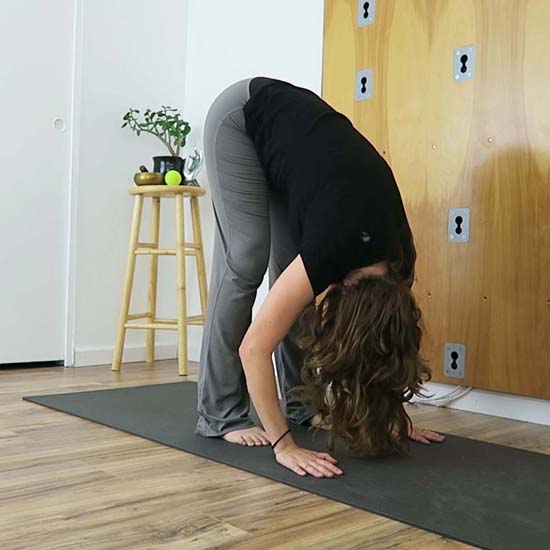 yoga teacher demonstrating forward fold with knees bent
