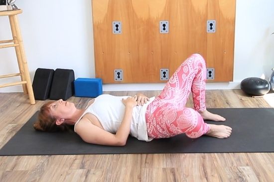 on a yoga mat, knees bent feet on floor, with a tennis ball under right glute