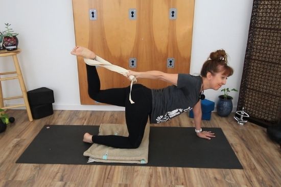 woman demonstrating tiger tail yoga pose with a yoga strap