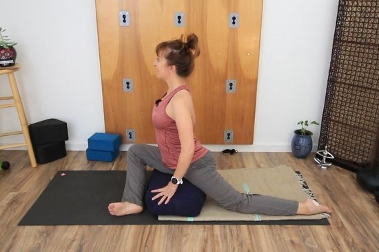 yoga teacher demonstrating pigeon pose with a bolster, Pink top, grey pants